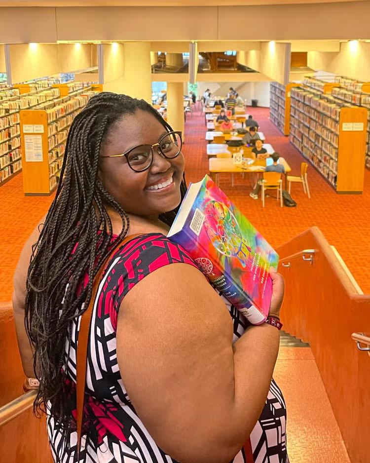 Lellow Sedio holds a book in a library.